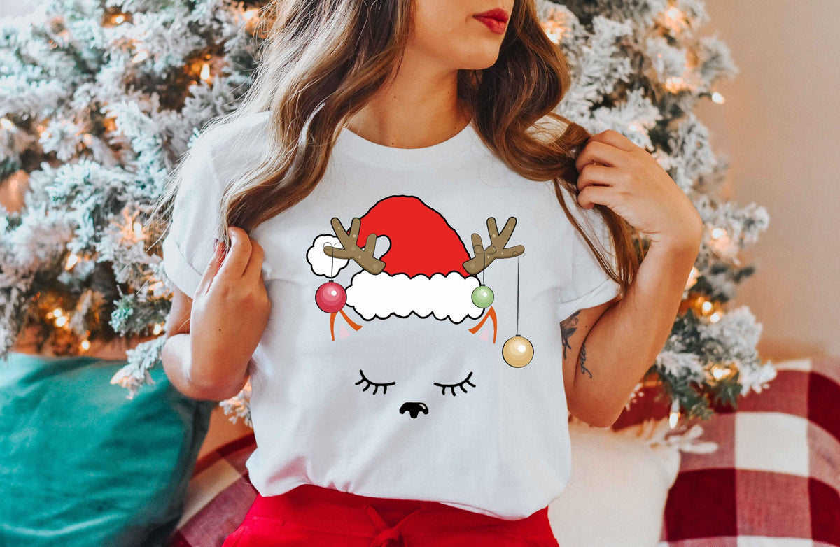 a woman wearing a santa clause t - shirt in front of a christmas tree